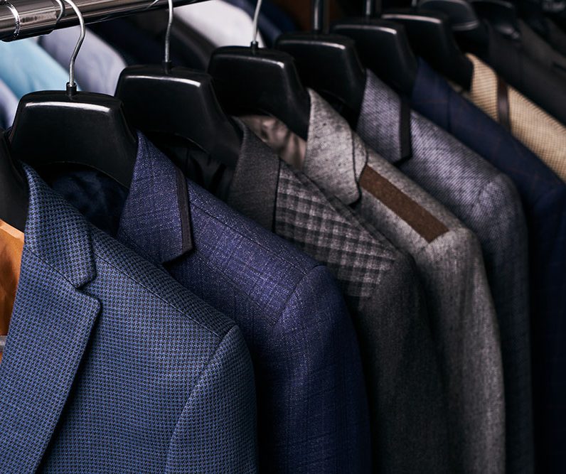 Mens suits in different colors hanging on hanger in a retail clothes store, close-up